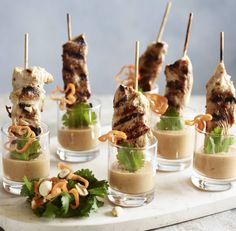 several skewered meats with sauce and garnishes in small glass cups