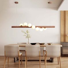 a dining room table and chairs with lights hanging from the ceiling above it, in front of a white wall