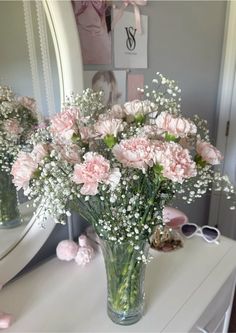 pink carnations and baby's breath in a vase on a dressing table