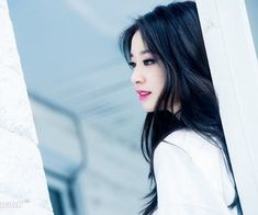 a woman with long black hair standing next to a wall