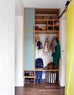 an open closet with clothes, shoes and bags on shelves next to a yellow curtain