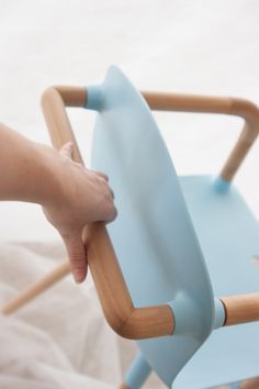 a child's hand is on the back of a blue chair with wooden legs