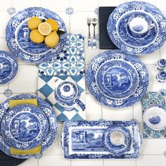 a blue and white table setting with plates, utensils and lemon wedges