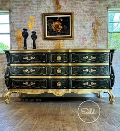 an ornate dresser with gold trim and black paint on it, in front of a brick wall