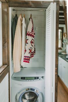 a washer and dryer in a small room with clothes hanging on the wall