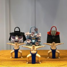 three small figurines are on display in front of a handbag and purse