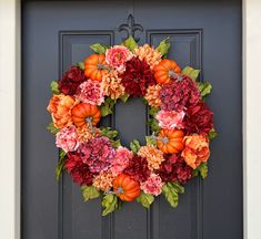 a wreath with flowers and pumpkins is hanging on the front door to welcome guests