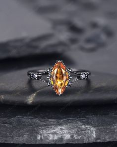 an orange topazte ring with filigrees sits on a black rock