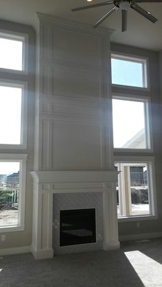 an empty living room with three windows and a ceiling fan in the middle of it