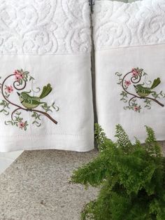 two white towels with birds on them sitting next to a plant and potted plant