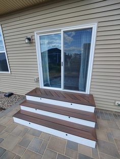 a wooden bench sitting on top of a patio next to a door and window sill