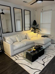 a living room with white couches and mirrors on the wall above it's coffee table