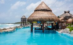 people are sitting at the edge of a swimming pool with thatched huts on it