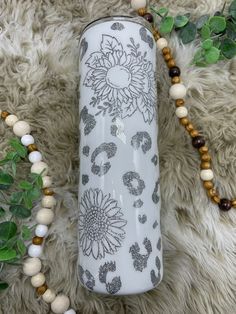 a white vase sitting on top of a rug next to a beaded necklace and flowers