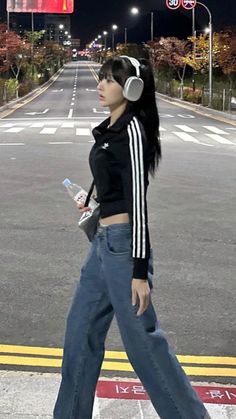 a woman walking down the street with headphones in her ears, wearing jeans and a crop top