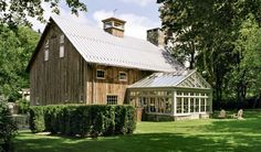 a large wooden barn sitting in the middle of a lush green field next to trees