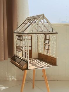 a doll house sitting on top of a wooden tripod in front of a window