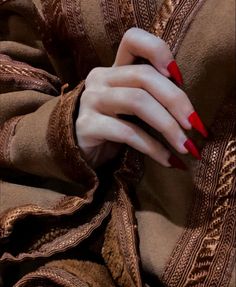 a woman's hand with red nail polish on her nails and brown sweater over her shoulders