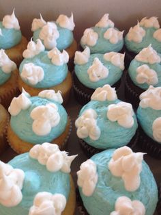 cupcakes with blue frosting and white flowers on them are displayed in a box