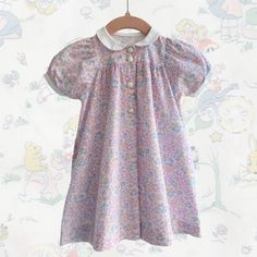 "A sweet little vintage baby dress in a lovely floral print. The dress fastens with buttons at the front and has a sweet little Pier Pan collar.  Very good vintage condition.  Measurements: Chest: 22\" Waist: free Length: 16\" Sizes for vintage childrenswear are approximate and it is best to take a look at the measurements to ascertain size. Measurements are for the garment, so I'd advise measuring a similar garment and comparing the measurements to get a good impression of fit." Spring Doll Collar Dress With Buttons, Cute Spring Dress With Button Closure, Cute Doll Collar Dress With Buttons, Cute Daywear Dresses With Peter Pan Collar, Cute Vintage Spring Dress For Daywear, Cute Vintage Dress For Spring Daywear, Cute Daywear Dresses With Buttons, Cotton Dress With Peter Pan Collar And Buttons, Vintage Floral Print Dress For Tea Party