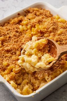 a casserole dish filled with macaroni and cheese, topped with a wooden spoon