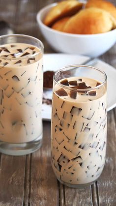 two glasses filled with liquid sitting on top of a wooden table next to plates and bowls