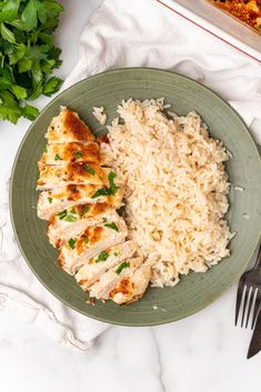 a green plate topped with chicken and rice next to a fork on top of a white table