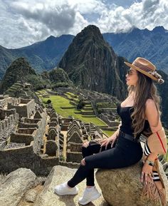 a woman sitting on top of a large rock next to a mountain with a valley in the background