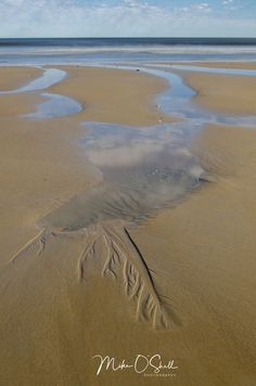 an empty beach with sand and water in the foreground, under a partly cloudy blue sky