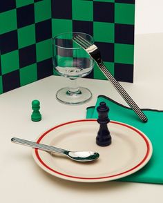 a plate with a fork on it next to a wine glass and some miniature chess pieces