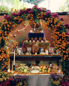 an outdoor altar with flowers and fruit on the table, surrounded by candles and decorations