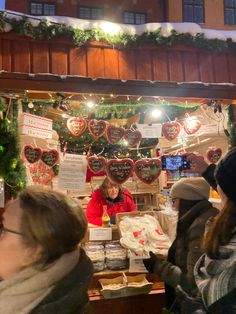 people standing in front of a christmas display with decorations on the wall and lights hanging above them