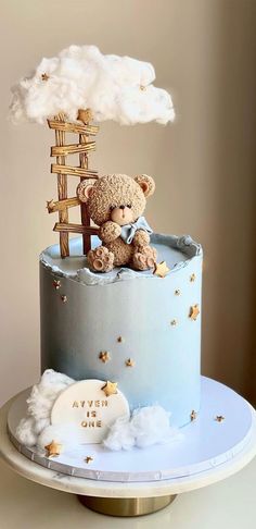 a teddy bear sitting on top of a blue and white cake with clouds in the background