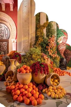 a table topped with vases filled with oranges and other fruit next to a wall