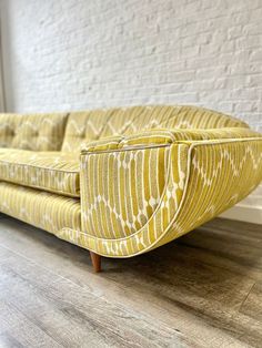 a yellow couch sitting on top of a hard wood floor next to a white brick wall