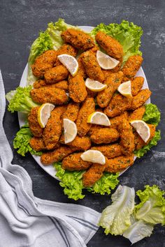 chicken wings with lemon wedges and lettuce leaves on a white plate next to a gray towel