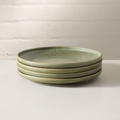 four green plates stacked on top of each other in front of a white brick wall