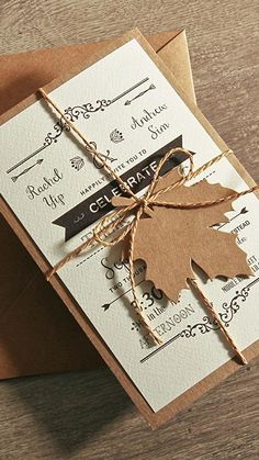 a card with a brown leaf tied to it on top of a wooden table next to a piece of paper