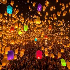 many people are flying lanterns in the night sky with colorful paper lanterns floating above them