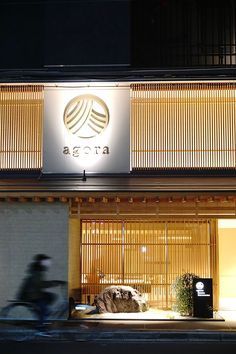 a person riding a bike past a building with bamboo blinds on it's windows