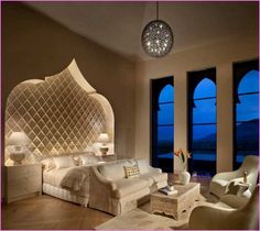 a bedroom with white furniture and large windows overlooking the ocean at night, is pictured in this image