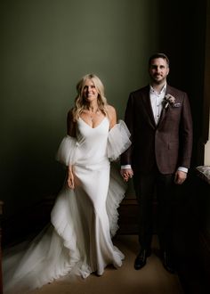 a man and woman standing next to each other in front of a green wall holding hands