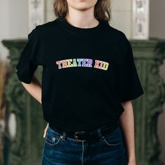 You love theater. I love theater. Why be embarrassed about the Theater Kid of it all? This colorful rainbow (perhaps even Pride-inspired!) theatre t shirt is perfect for everyone who's not afraid to talk about Wicked, Hamilton, or Dear Evan Hansen for hours. Wear to your next Broadway show or to see a musical on tour! .: 100% cotton (fiber content may vary for different colors) .: Medium fabric (5.3 oz/yd² (180 g/m .: Classic fit .: Tear-away label .: Runs true to size Pre-shrunk Cotton Rainbow T-shirt, Cotton T-shirt With Rainbow Print For Pride, Rainbow Cotton T-shirt, Pre-shrunk, Rainbow Cotton T-shirt Pre-shrunk, Cotton Slogan T-shirt For Pride, Pre-shrunk Cotton Rainbow Colored Tops, Pre-shrunk Cotton Rainbow Tops, Rainbow Colored Pre-shrunk Cotton Tops, Rainbow Pre-shrunk Cotton Top