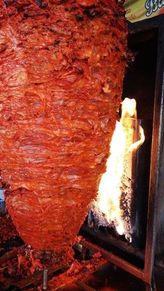 a large piece of meat is being cooked in an open fire pit with flames coming from it