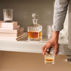 a person is holding a glass in front of a shelf with liquor bottles and glasses on it