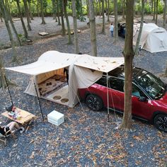 a red car parked in the woods next to a tent and picnic table with food on it