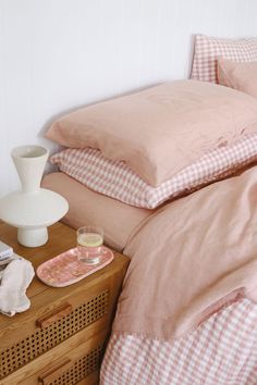 a bed with pink sheets and pillows on top of it next to a night stand