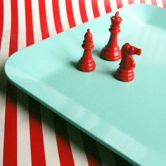 two red chess pieces sitting on top of a blue tray next to a striped table cloth