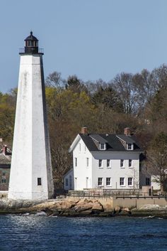 a white lighthouse sitting on top of a body of water next to a small house