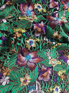 an embroidered fabric with colorful flowers and leaves on it's side, as well as green foliage